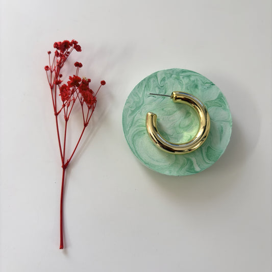 Gold hoop earring on a green marbled stand with red flowers on a white background