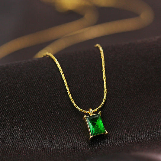 Gold necklace with a green gemstone pendant on a dark fabric background