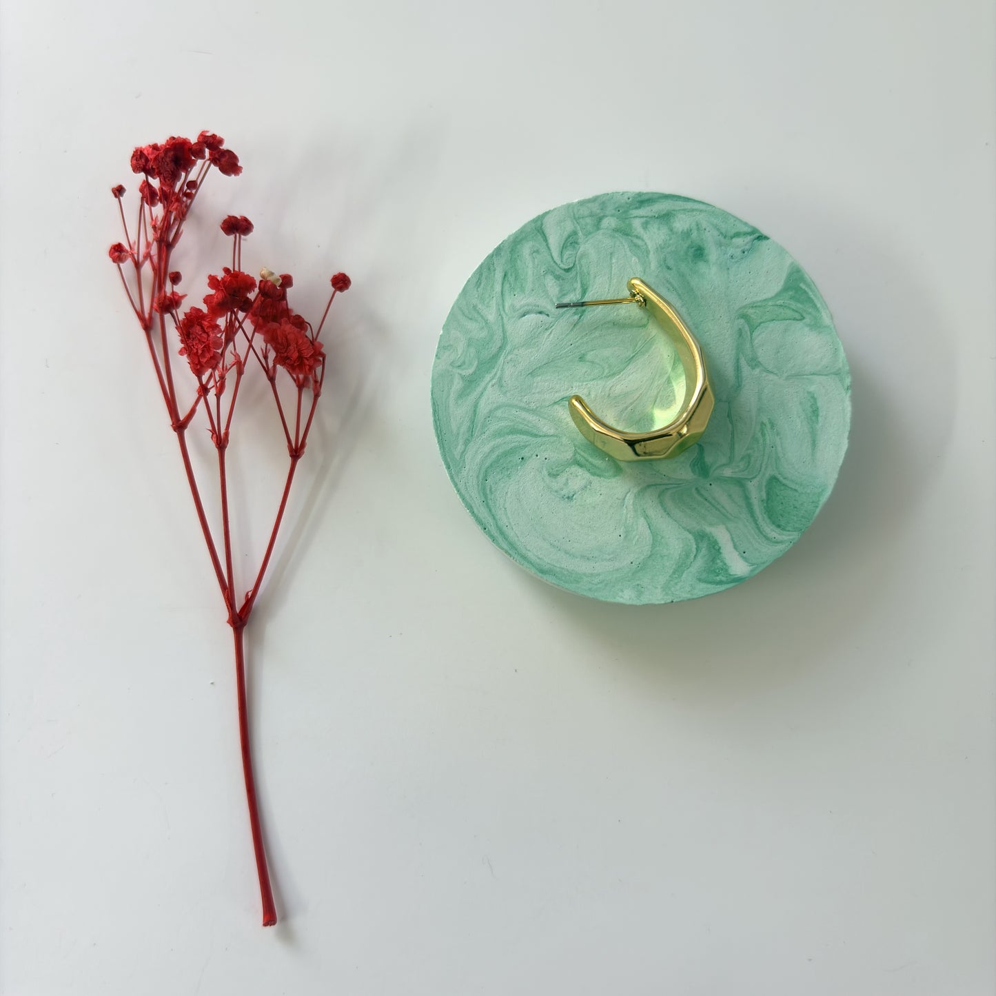 Green marbled ring holder with gold ring and red flowers on a white background