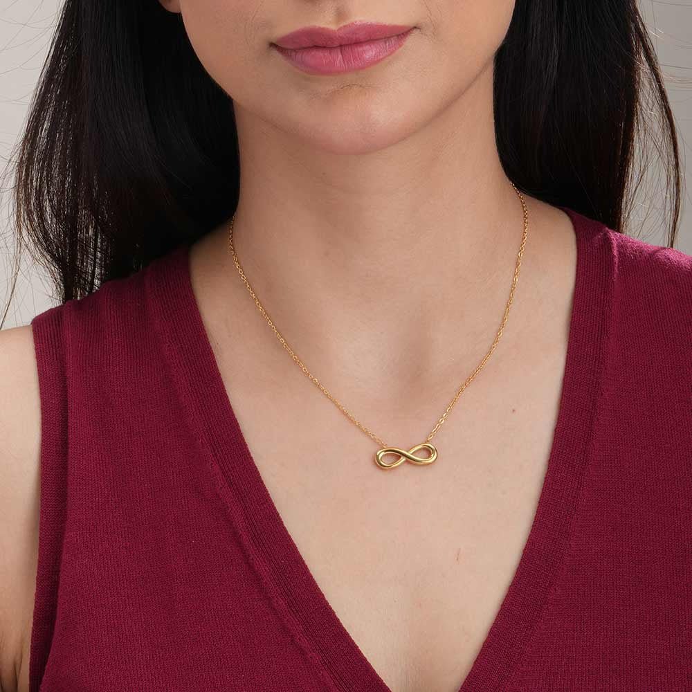 Woman wearing a gold necklace with an infinity symbol pendant.
