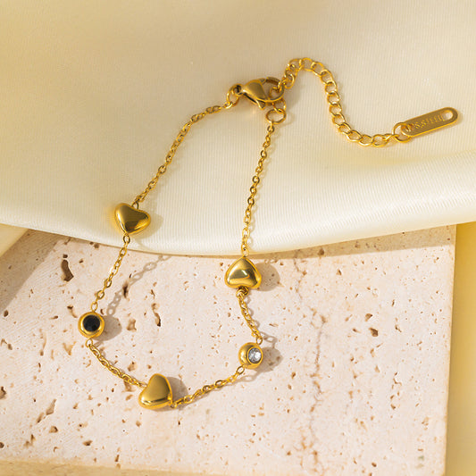 Gold bracelet with heart-shaped charms on a textured beige surface