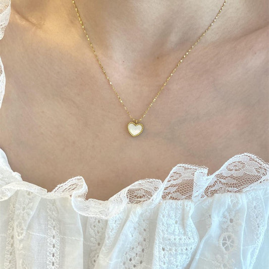 Gold necklace with a heart-shaped pendant worn by a person in a white lace top.