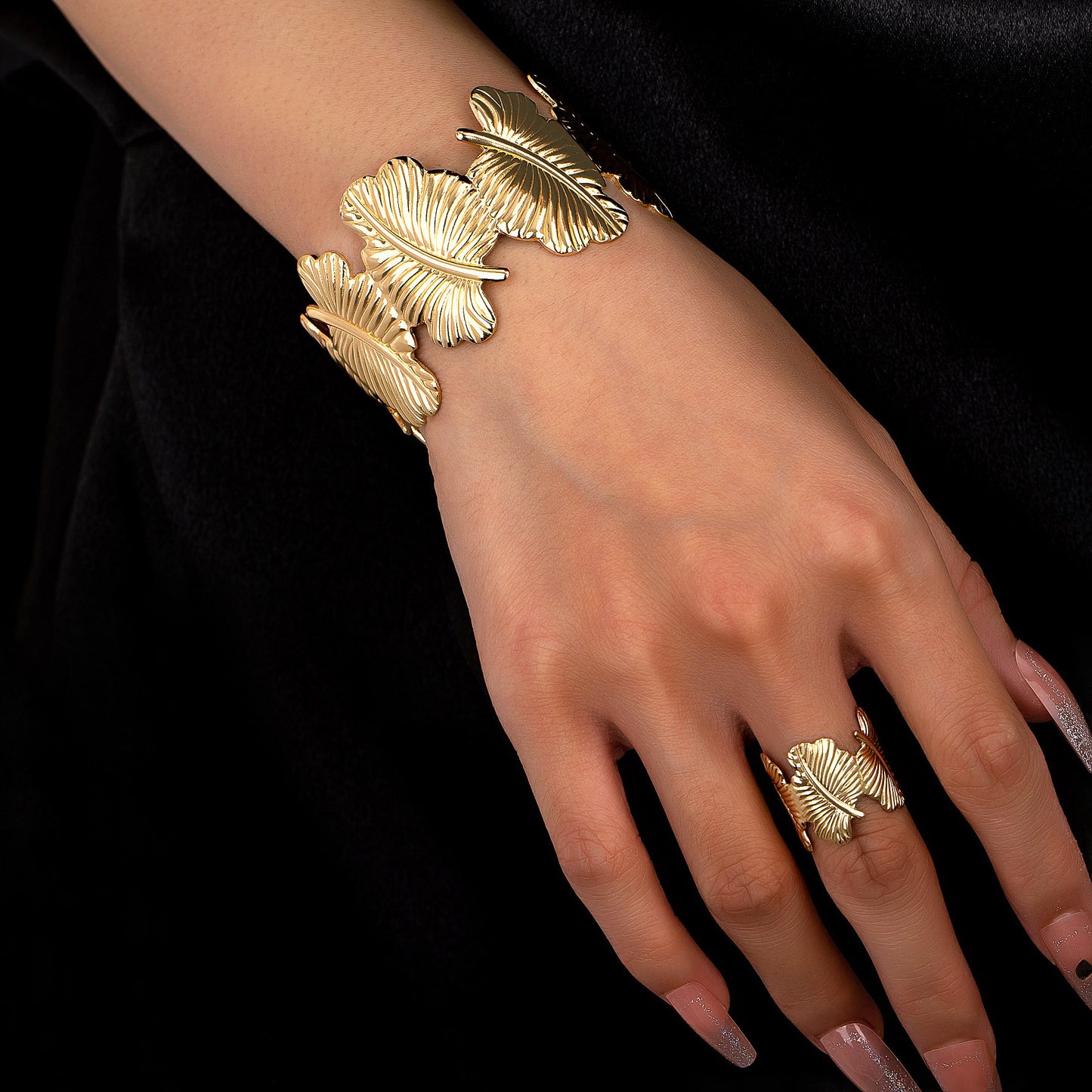 Gold leaf bracelet and ring on a hand against a black background