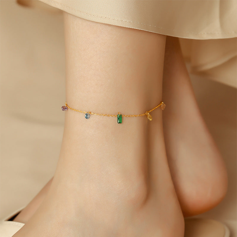 Gold anklet with colorful beads on a person's ankle against a neutral background