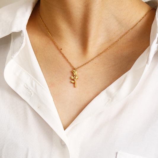 Gold necklace with a leaf pendant worn by a person in a white shirt.