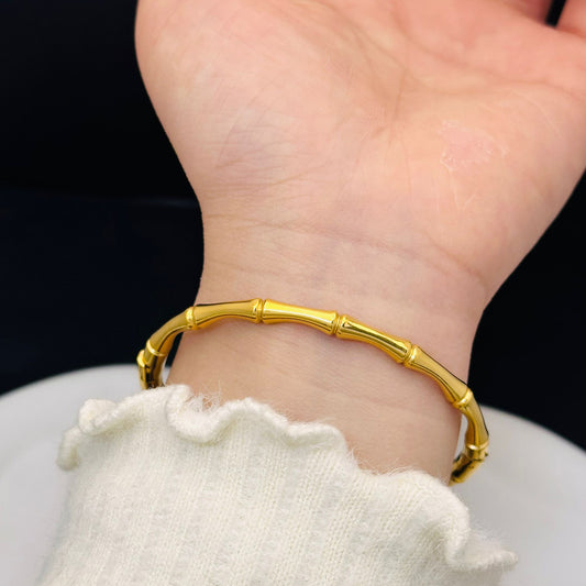 Gold bamboo-style bracelet on a wrist with a blurred background