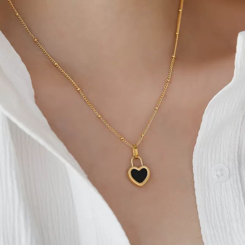 Gold necklace with a heart-shaped pendant worn by a person in a white top.