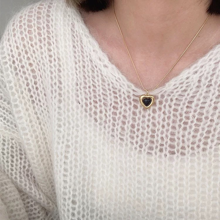 Necklace with a heart-shaped pendant worn by a person in a white textured garment.