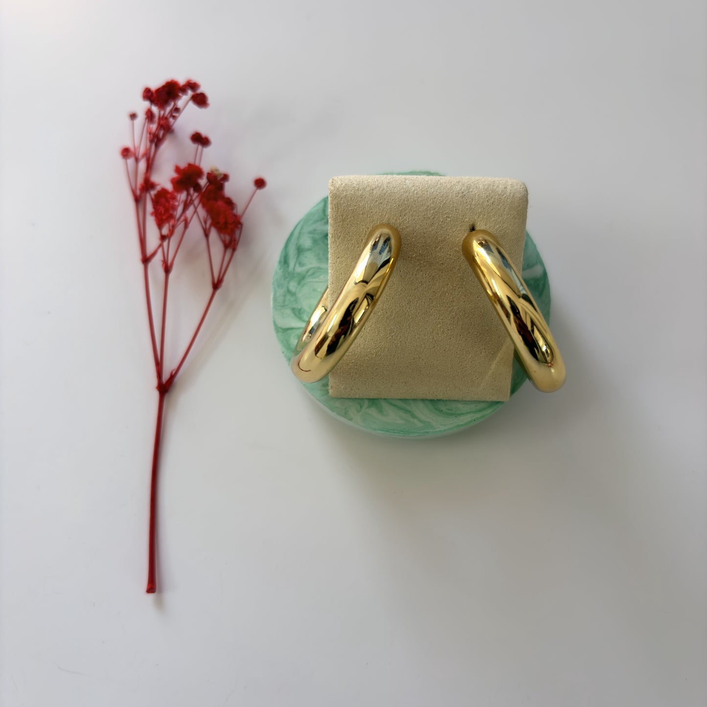 Gold hoop earrings on a green stand with a red flower on a white background