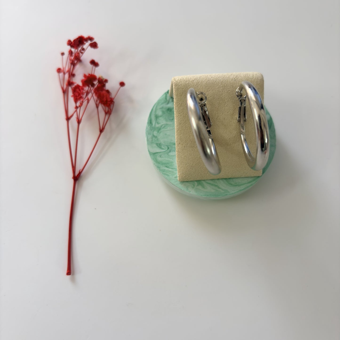 Silver hoop earrings on a green stand with a red flower on a white background