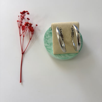 Silver hoop earrings on a green stand with a red flower on a white background