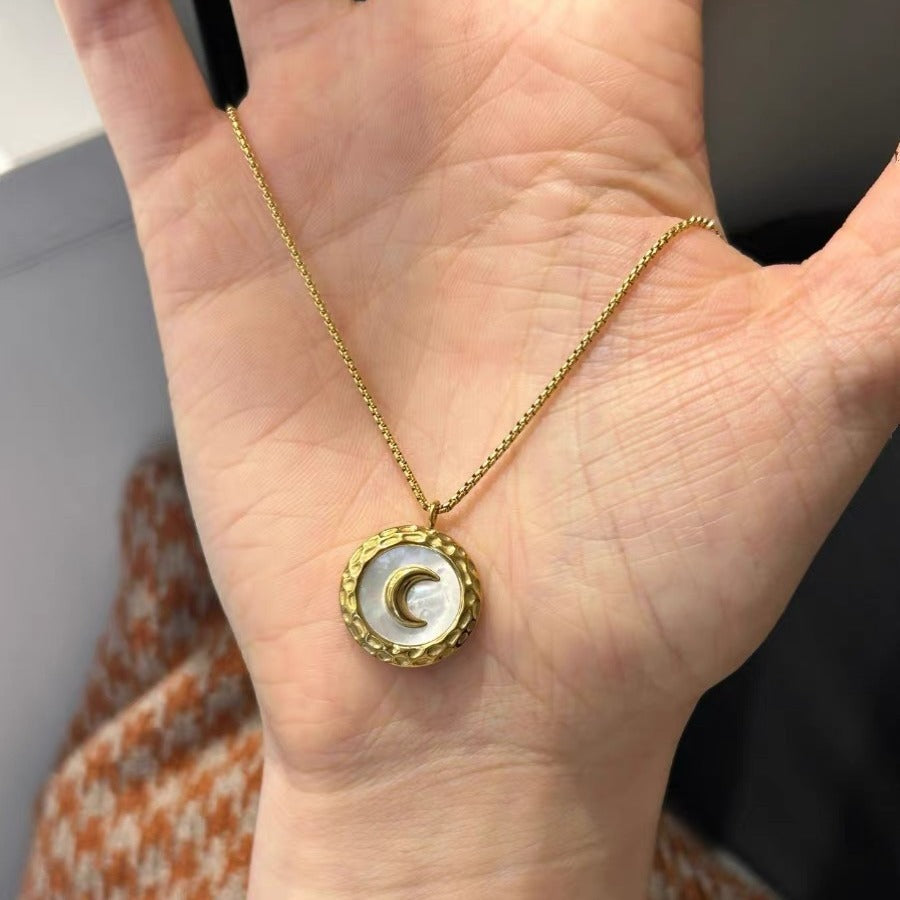 Gold necklace with a circular pendant featuring a moon design held in a hand.