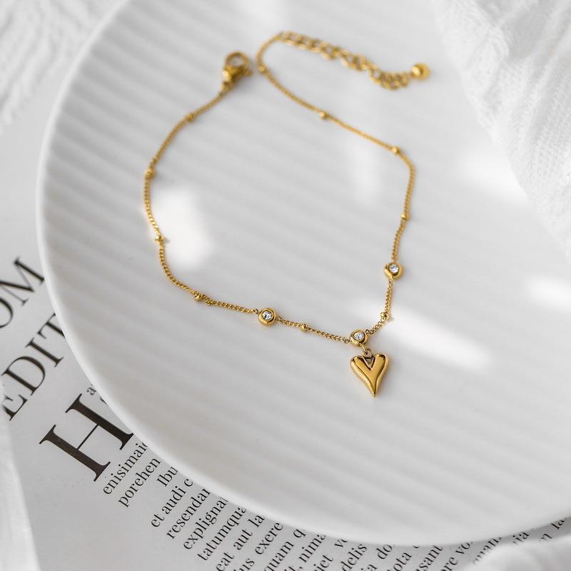 Gold bracelet with a heart charm on a white plate