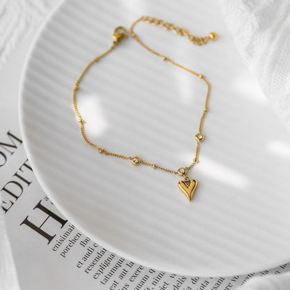 Gold bracelet with a heart charm on a white plate