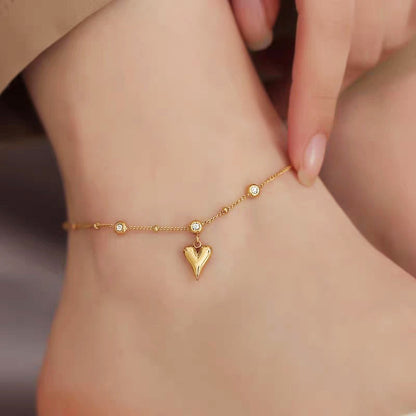 Gold anklet with a heart-shaped charm on a person's ankle.