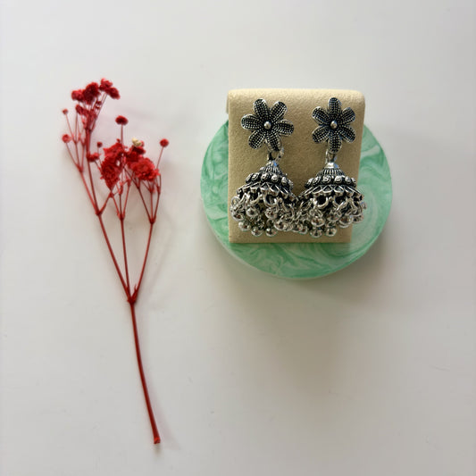 Silver floral earrings on a green stand with red flowers on a white background