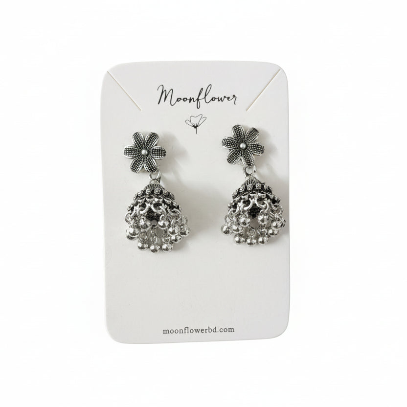 Pair of silver floral earrings on a 'Moonflower' branded card held by a gloved hand.