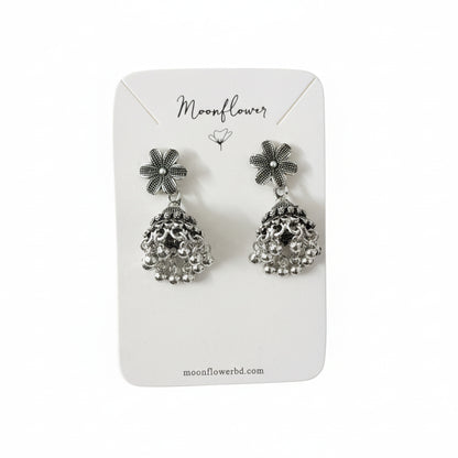 Pair of silver floral earrings on a 'Moonflower' branded card held by a gloved hand.