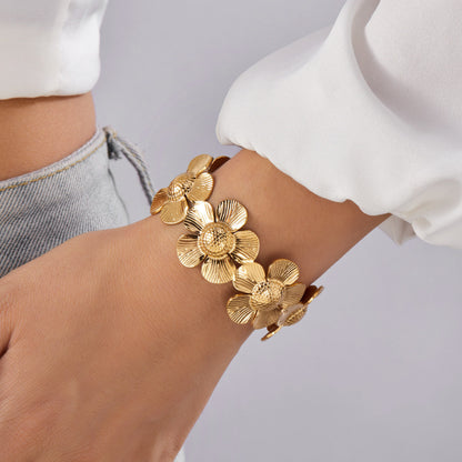 Gold floral bracelet on a wrist with a neutral background