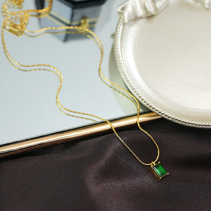 Gold necklace with a green pendant on a dark fabric background
