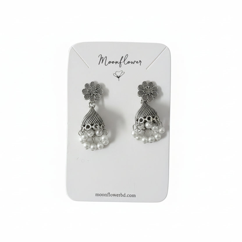 Silver earrings on a 'Moonflower' branded card held by a black gloved hand.