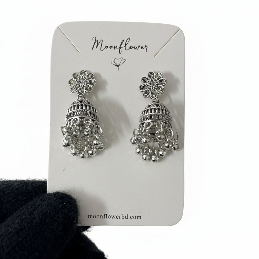 Silver floral earrings on a 'Moonflower' branded card held by a gloved hand.