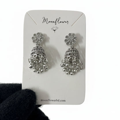 Silver floral earrings on a 'Moonflower' branded card held by a gloved hand.