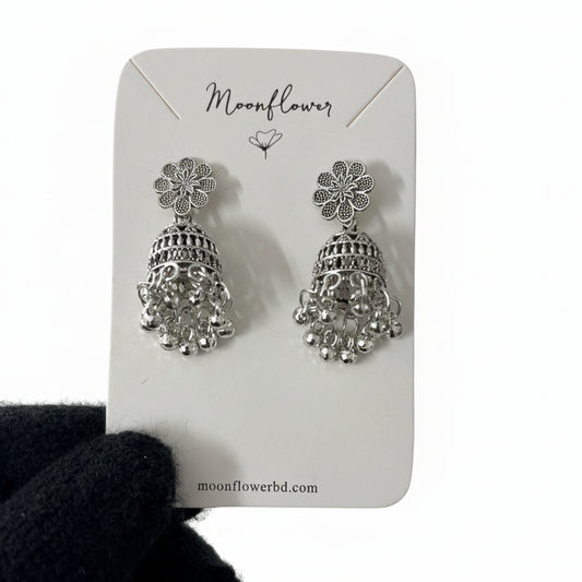 Silver floral earrings on a 'Moonflower' branded card held by a gloved hand.