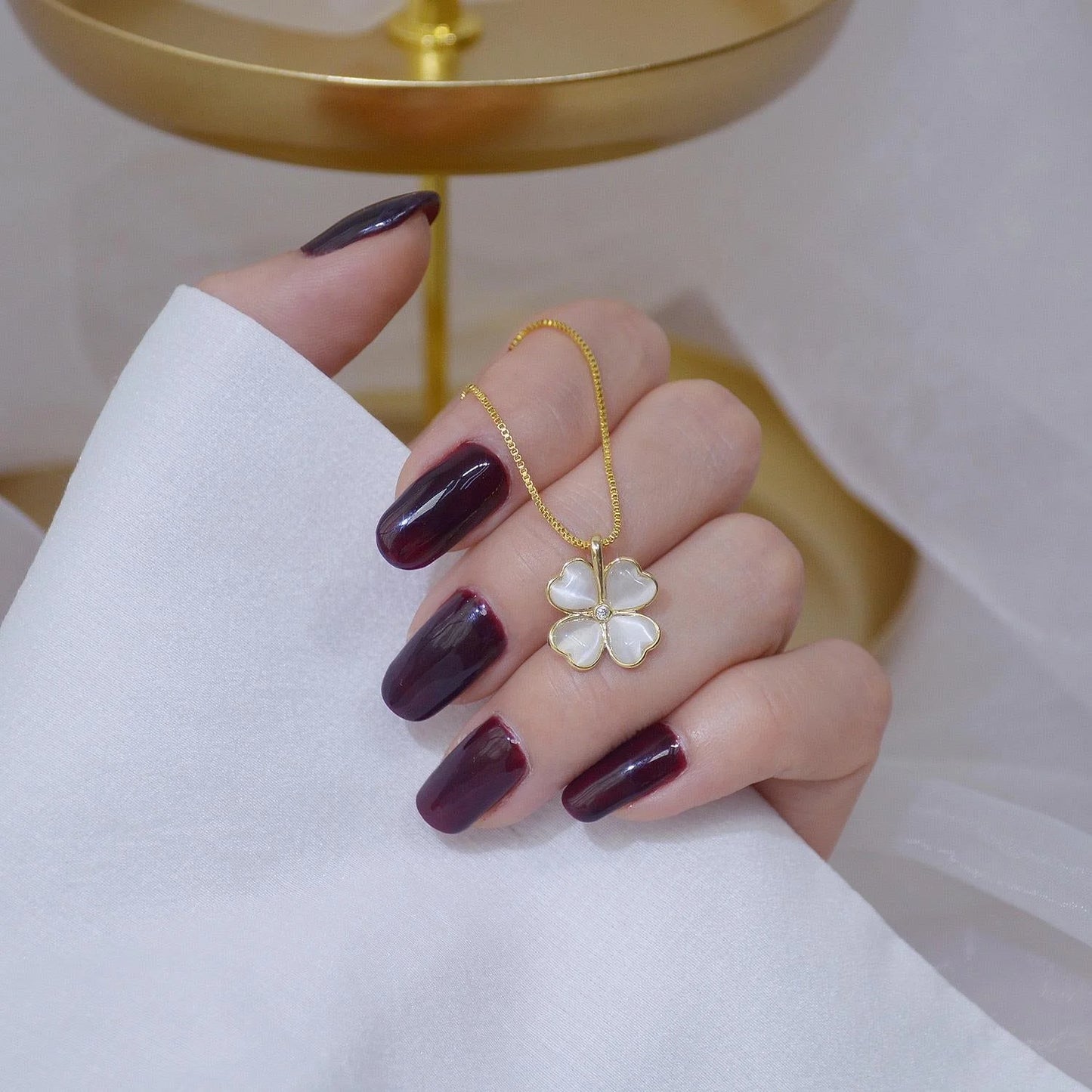 Hand wearing a gold necklace with a white pendant on a white background