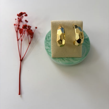 Gold earrings on a green stand with a red flower on a white background
