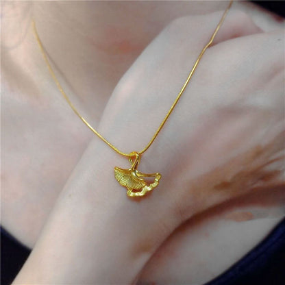 Gold necklace with a ginkgo leaf pendant on a person's wrist.