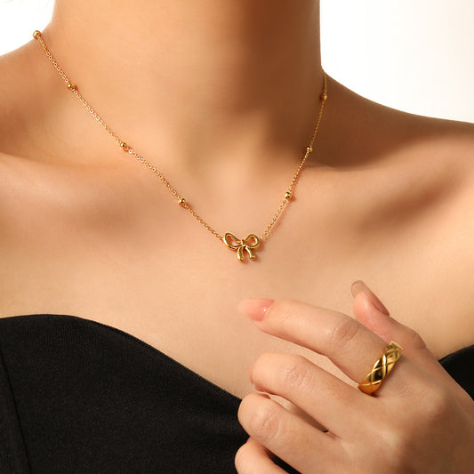 Gold necklace with a bow pendant worn by a person, with a hand wearing a matching gold ring.
