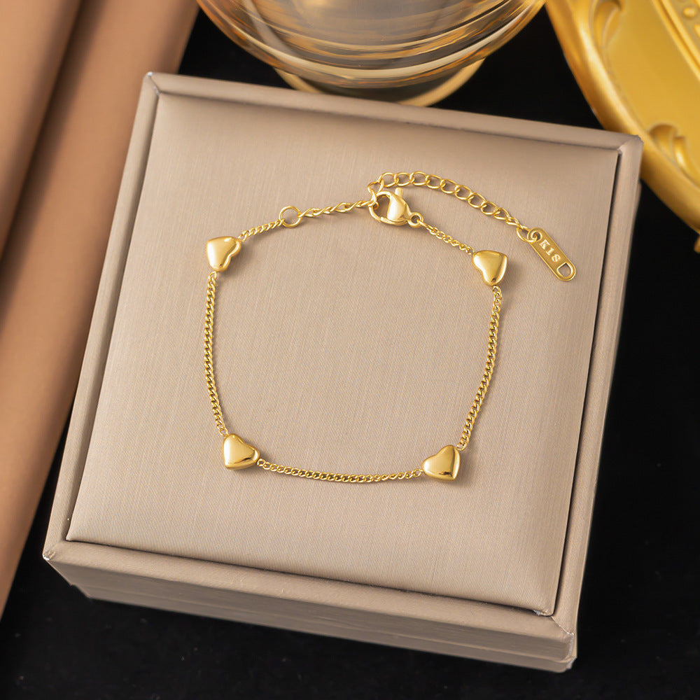 Gold bracelet with heart-shaped charms on a beige jewelry box