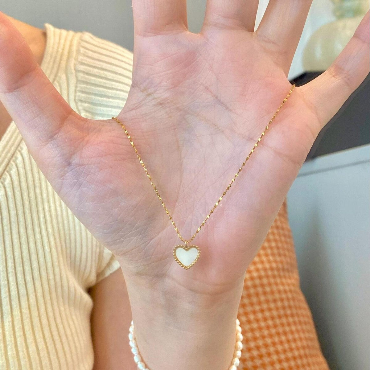 Hand wearing a gold necklace with a heart-shaped pendant