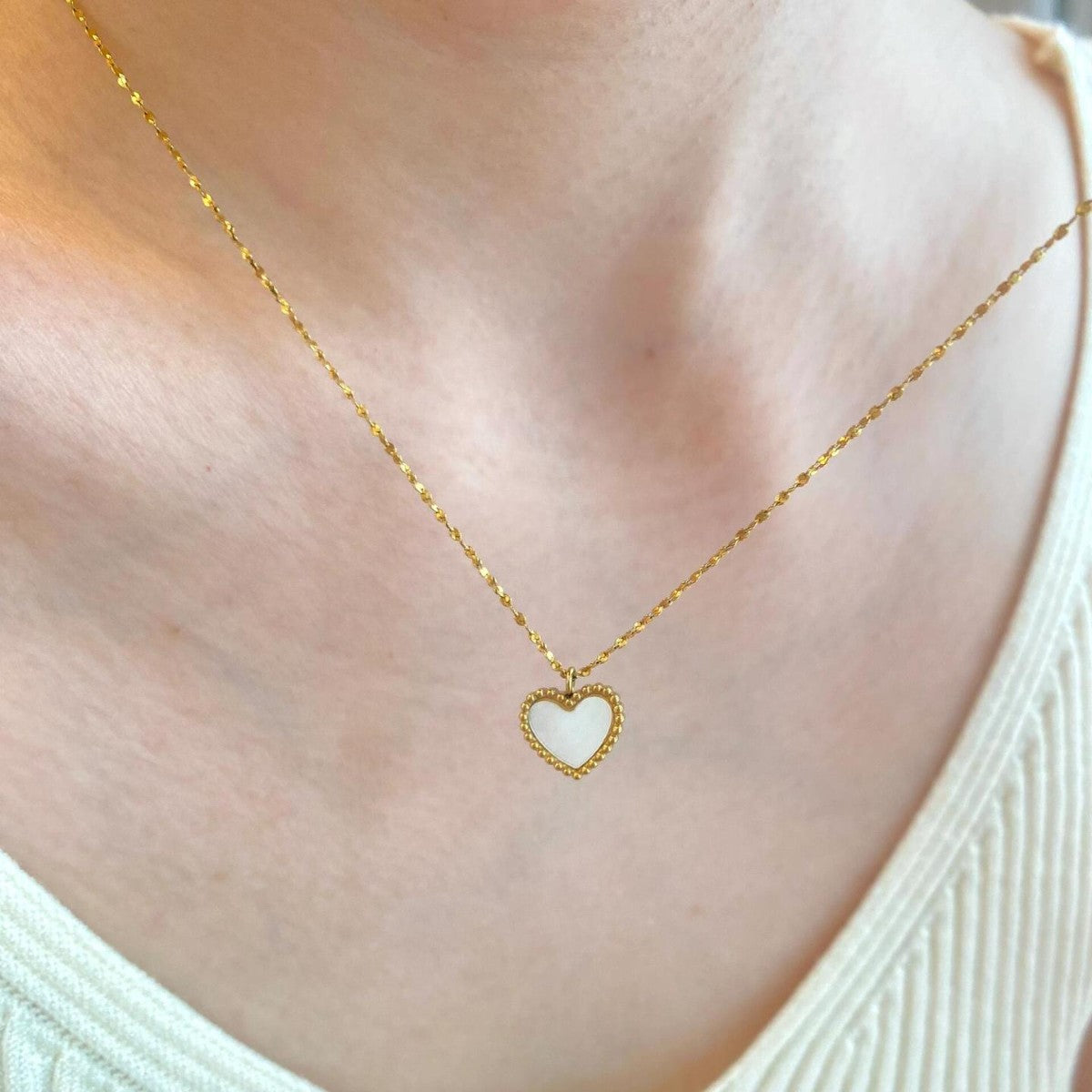 Gold necklace with a heart-shaped pendant on a person wearing a white top.