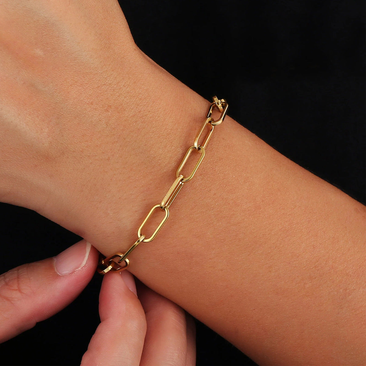 Gold chain bracelet on a wrist with a black background