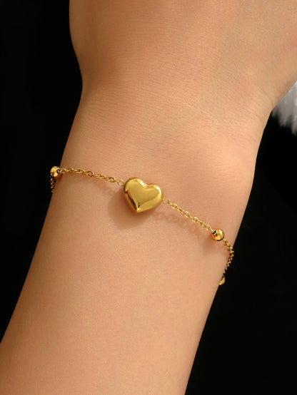 Gold heart-shaped bracelet on a wrist against a black background