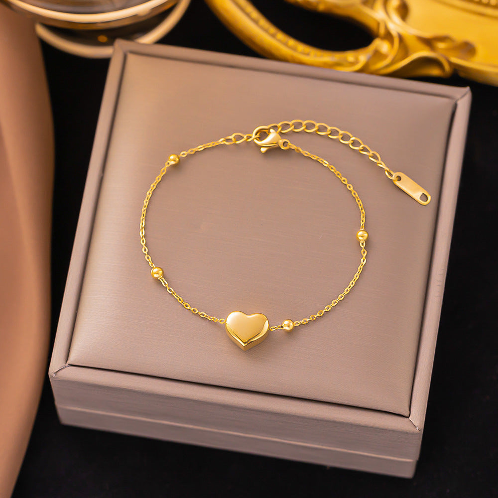 Gold bracelet with a heart charm on a gray jewelry box