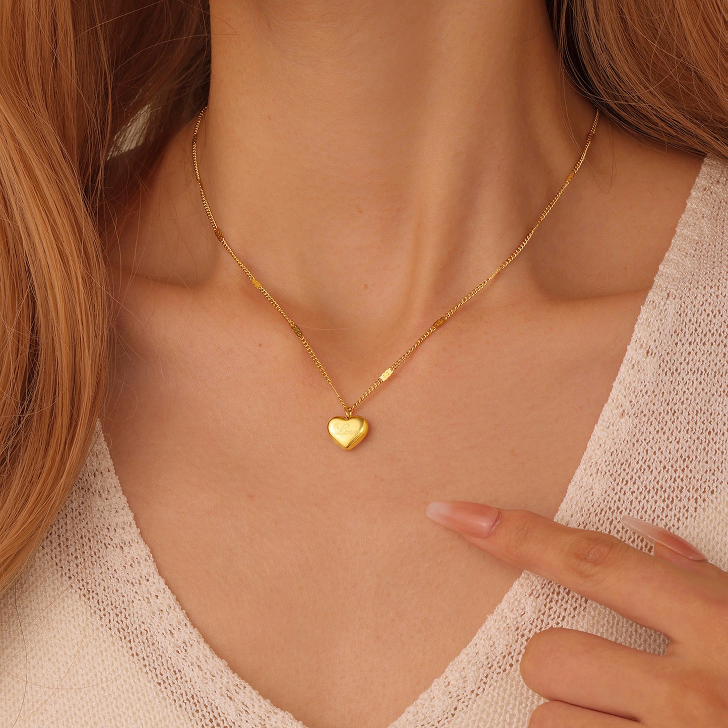 Gold heart-shaped necklace worn by a person, with a hand pointing to it.