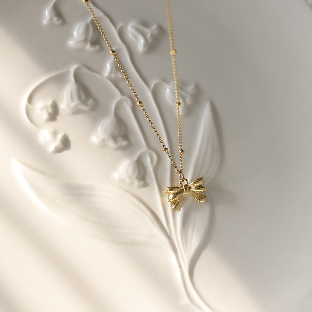 Gold bow-shaped necklace on a decorative white surface