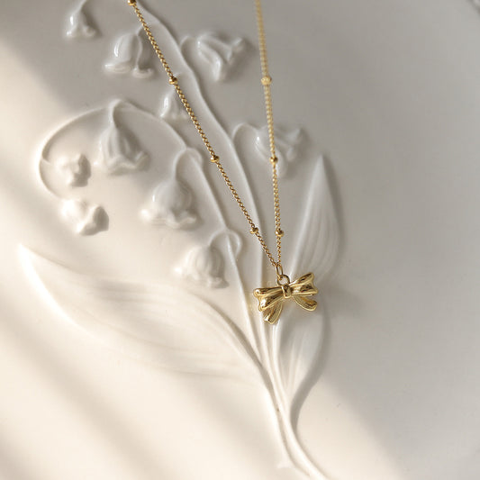 Gold bow-shaped necklace on a decorative white surface