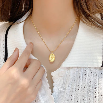 Gold necklace with a pendant on a mannequin, with a hand pointing to it.