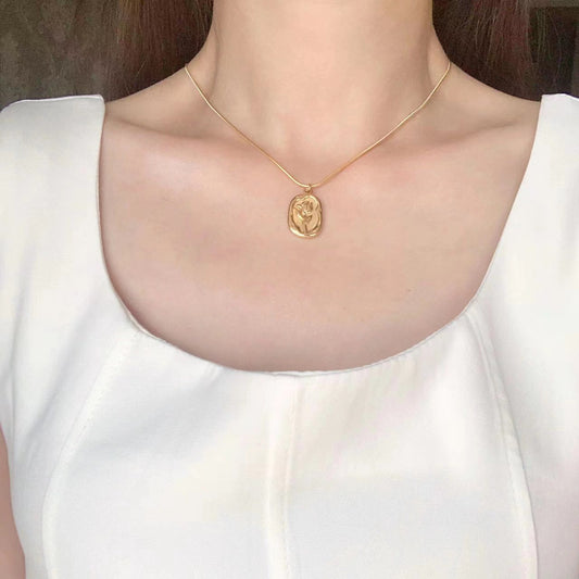 Gold necklace with a pendant worn by a person in a white top.