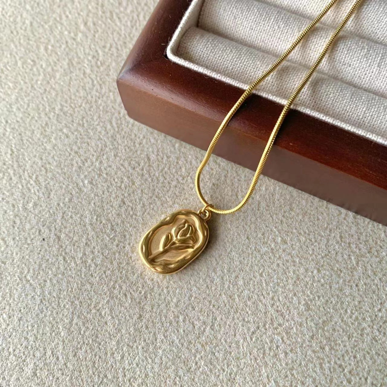 Gold necklace with a leaf pendant on a textured surface