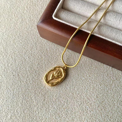 Gold necklace with a leaf pendant on a textured surface