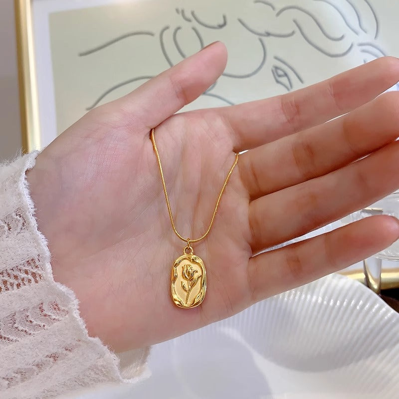 Gold necklace with a pendant on a hand against a neutral background