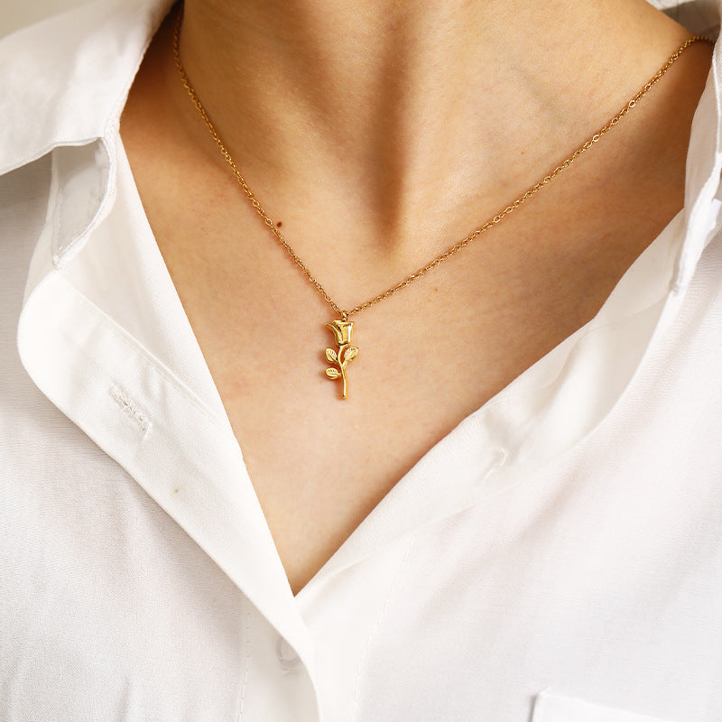 Gold necklace with a leaf pendant worn by a person in a white shirt.