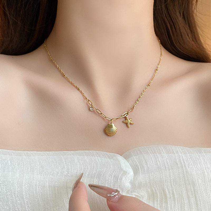 Gold necklace with shell and star charms on a person wearing a white top.