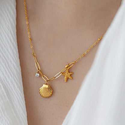 Gold necklace with shell and starfish charms on a person wearing a white top.