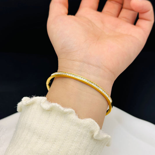 Gold bracelet with clear stones on a wrist against a black background